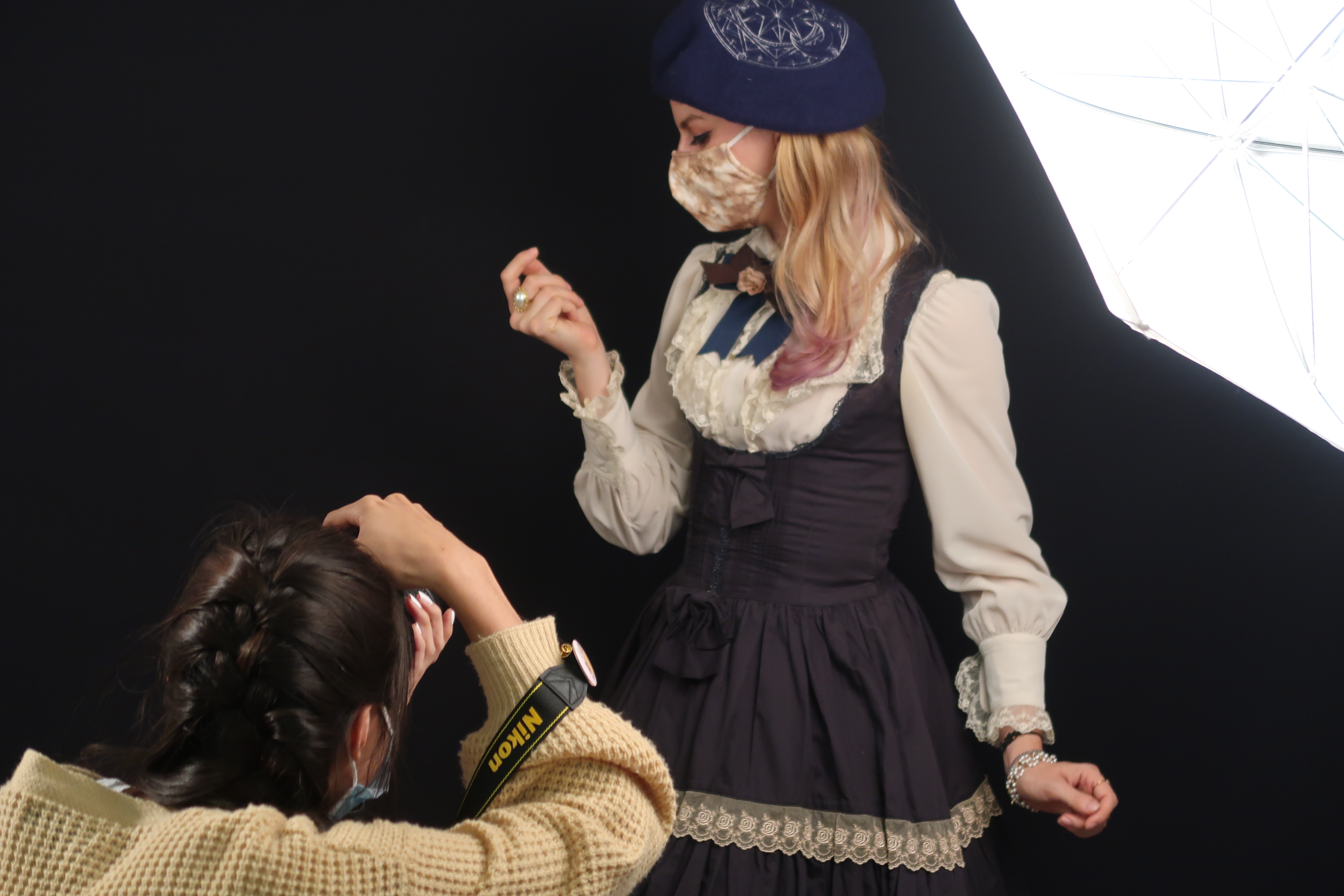 Student in braid taking photo of a student posing with hand to face and wearing a white ruffle blouse and black cinched dress.